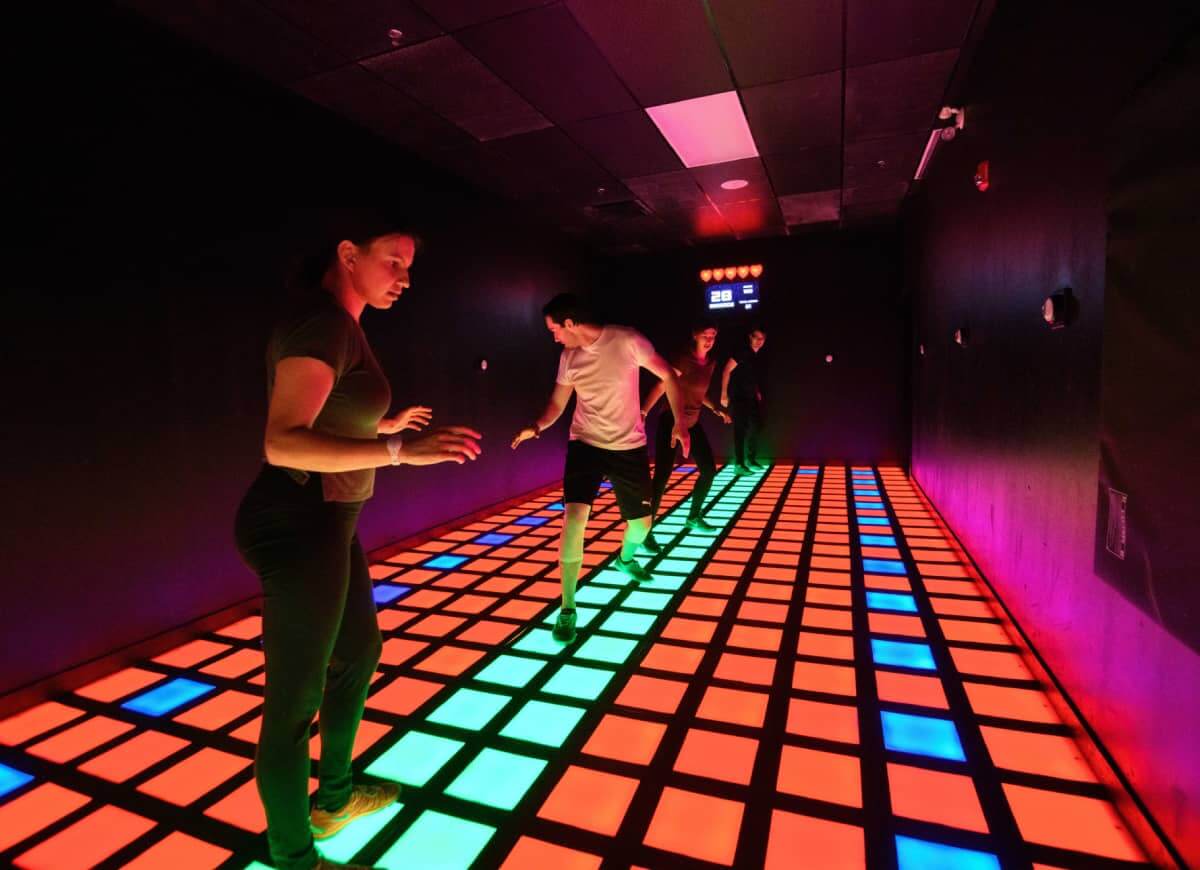 Four players moving together across a full-size illuminated Mega Grid floor